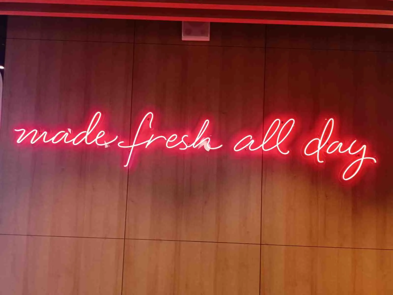 Красная неоновая надпись made fresh all day на деревянной стене KFC
